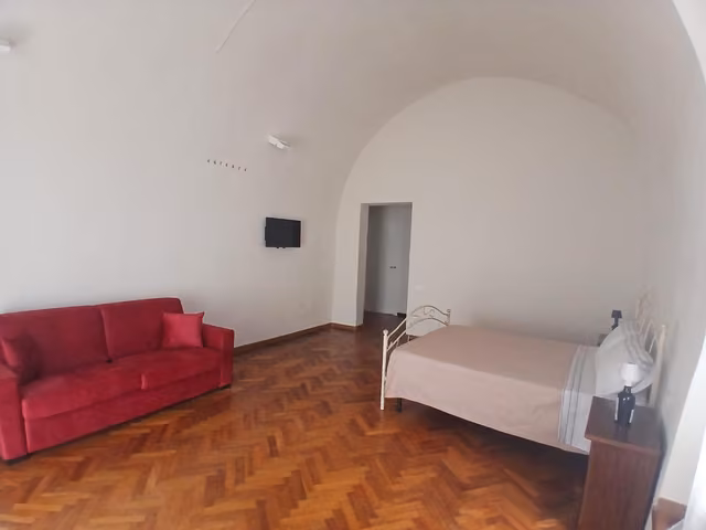 Soggiorno con divano rosso e letto della suite